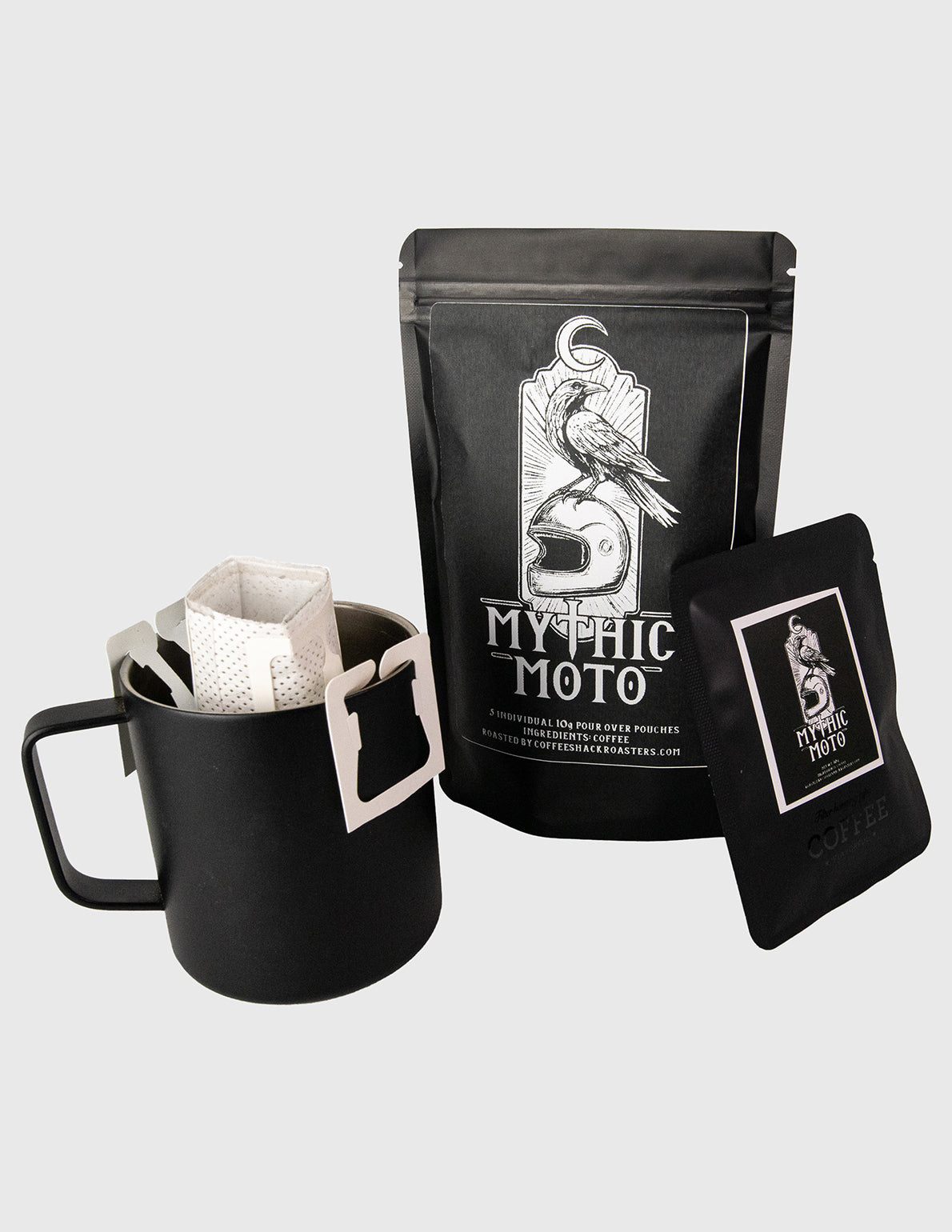 Black coffee bag, black mug with filter, and black coaster featuring 'Mythic Moto' branding on a light gray background. Travel Coffee pour over 
