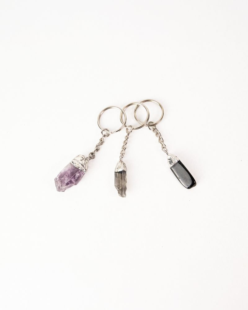 Three keychains with crystal pendants on a white background. Protection Stone, Guardian Bell, Mythic Moto, Her Two Wheels