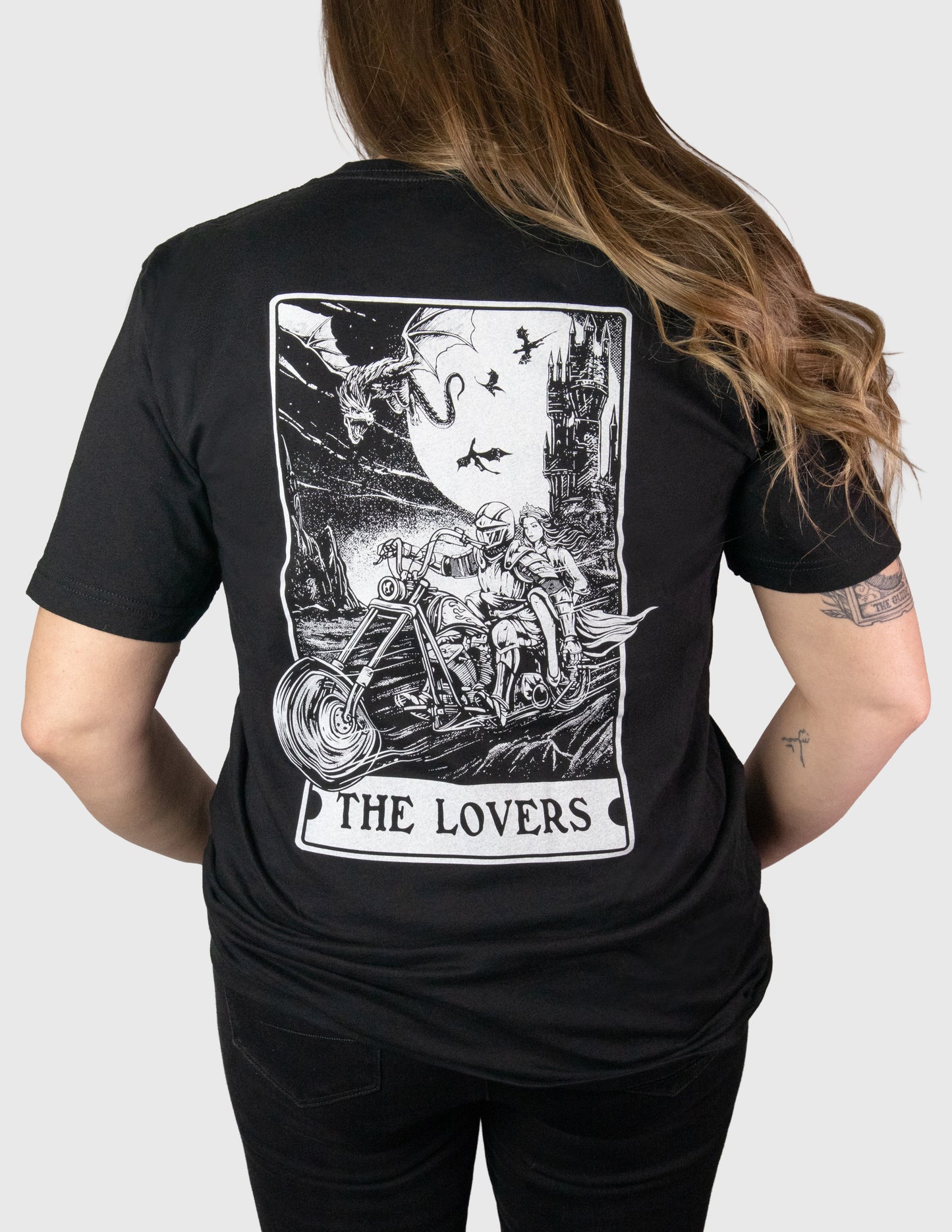 Woman wearing a black t-shirt with 'The Lovers' tarot card design on the back. Her Two Wheels