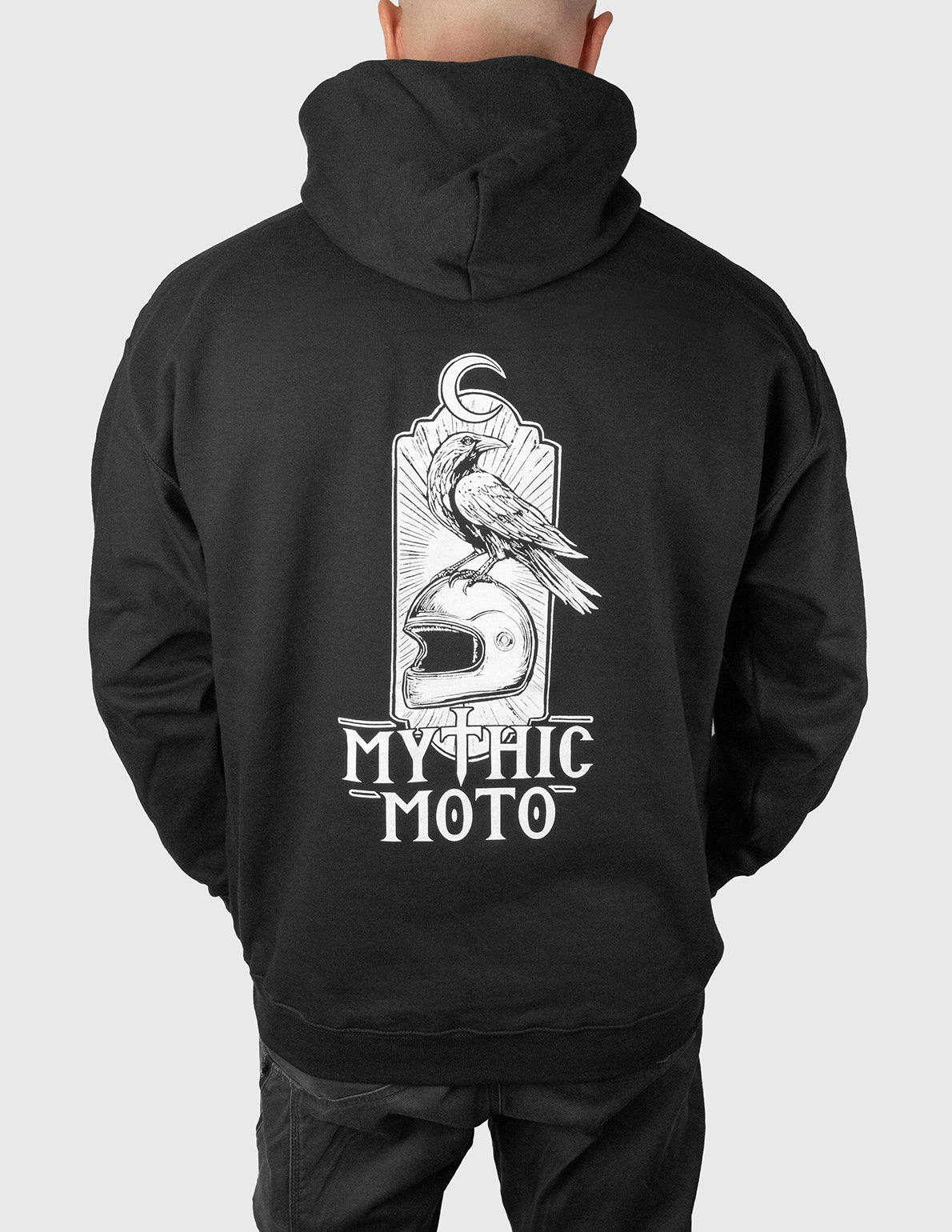 Man wearing a black hoodie with 'Mythic Moto' design on the back against a white background