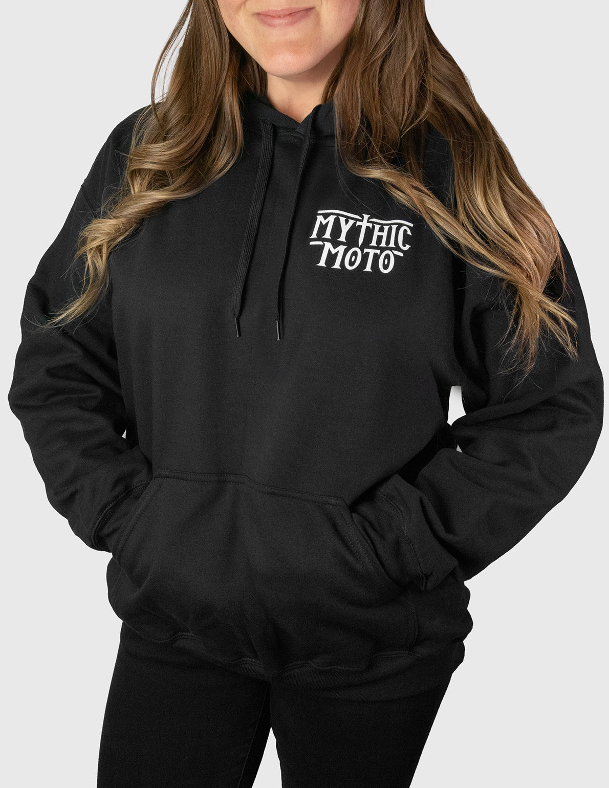 Woman wearing a black hoodie with 'Mythic Moto' logo on a white background
