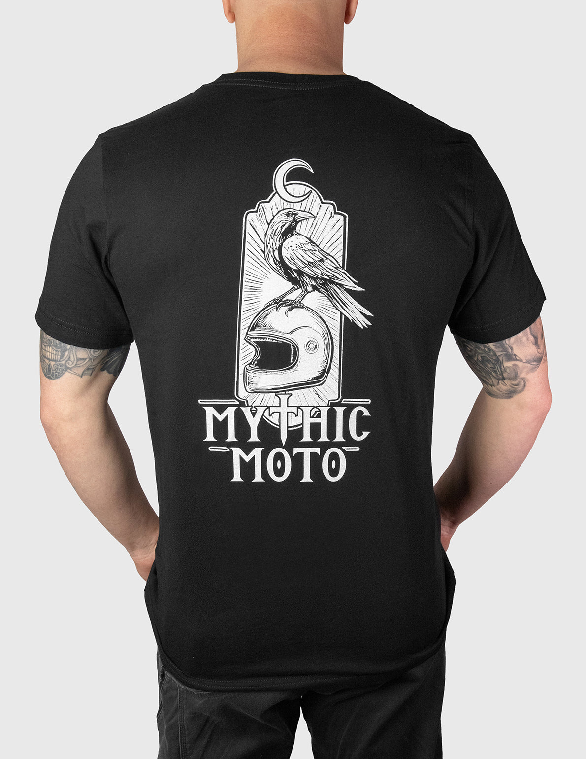 Person wearing a black t-shirt with 'Mythic Moto' design on the back, standing against a plain background.
