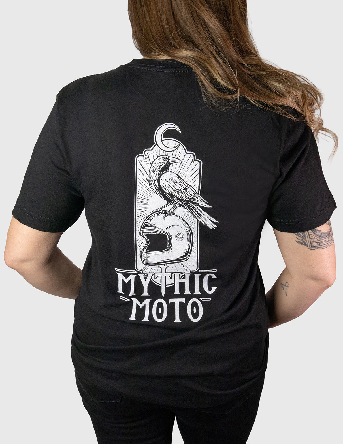 Woman wearing a black t-shirt with 'Mythic Moto' design on the back. Her Two Wheels