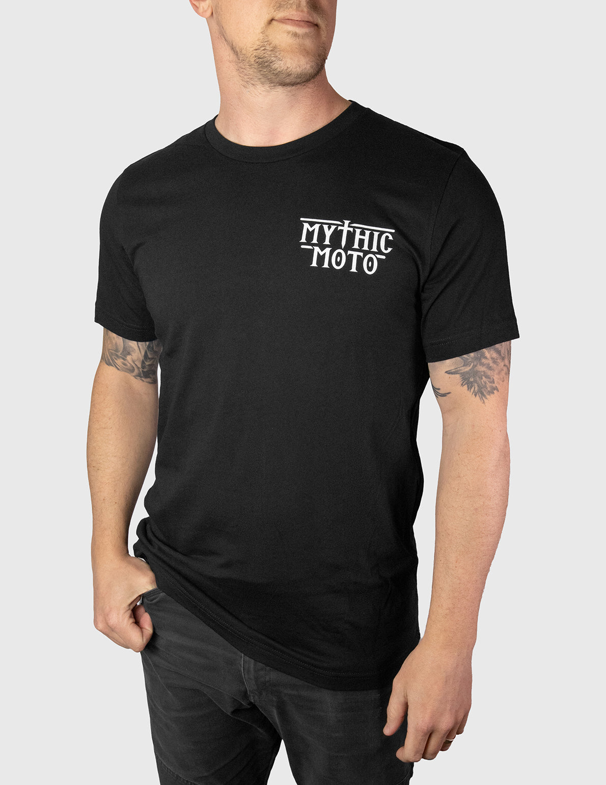 Person wearing a black t-shirt with 'Mythic Moto' logo on a plain background