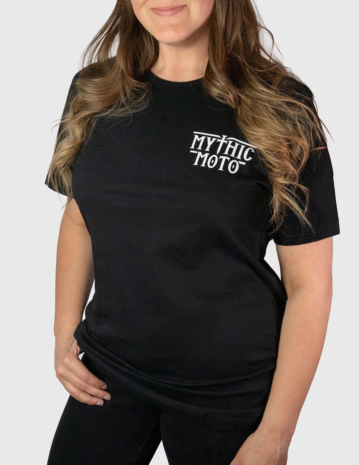 Woman wearing a black t-shirt with 'MYTHIC MOTO' text on a white background. Her Two Wheels